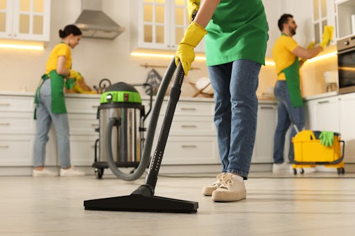 An image showing professional cleaners working, one using a hoover in the foreground.